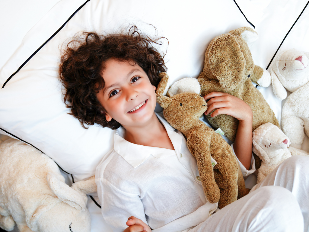 Kid in bed hugging soft toys from Carter & White